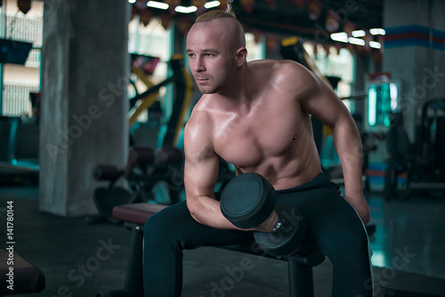 European strong athletic man make exercise with the dumbbells in the gym.