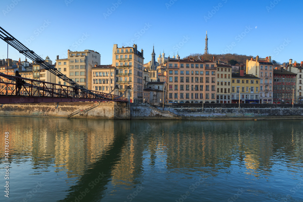 Fototapeta premium Pedestrian walking over Passerelle Saint-Vincent, crossing the Saone river, at dawn. Lyon, France.