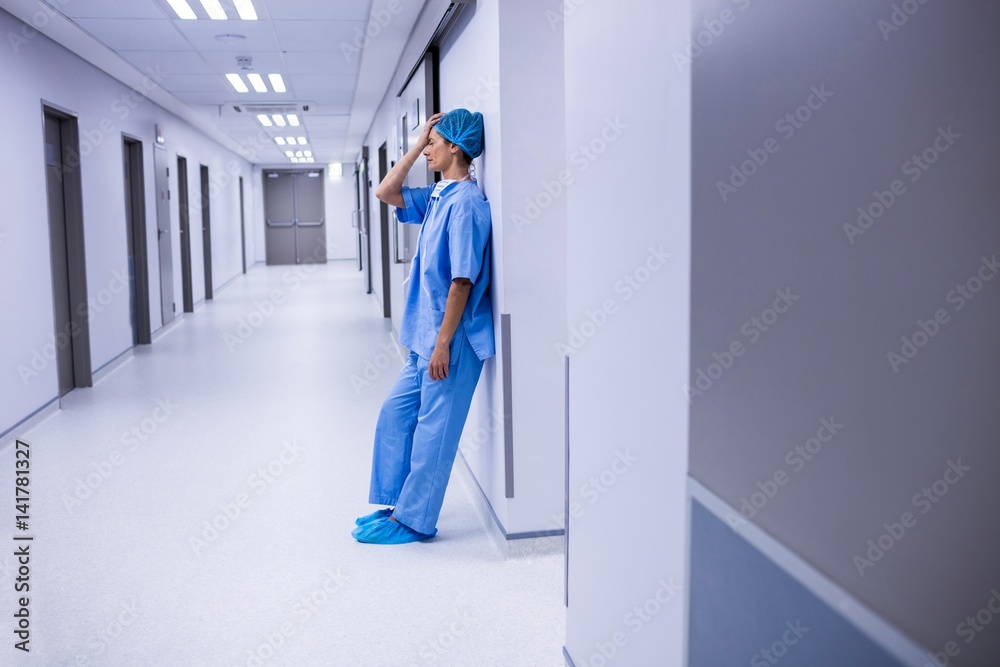 Sad surgeon leaning on wall in corridor
