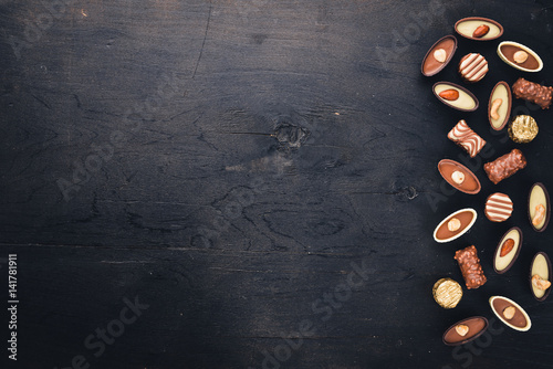 Assortment of chocolates with nuts. Black and milk chocolate. Wooden on the black surface. Top view.