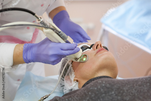 Therapist beautician makes a laser rejuvenation for the Woman by apparatus in a beauty salon.