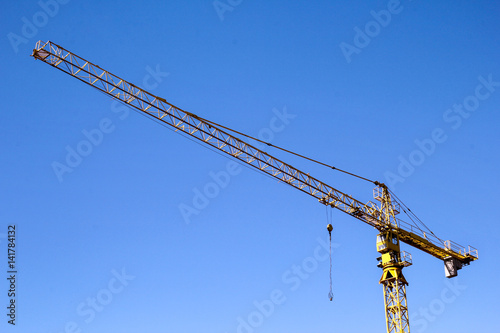 Yellow crane hoist. Yellow crane hoist with blue sky in the background. Hoisting crane against a background sky. Yellow construction tower crane against blue sky.