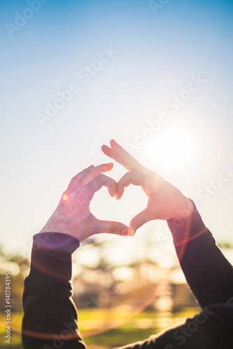 Heart from hands in the background of the sun