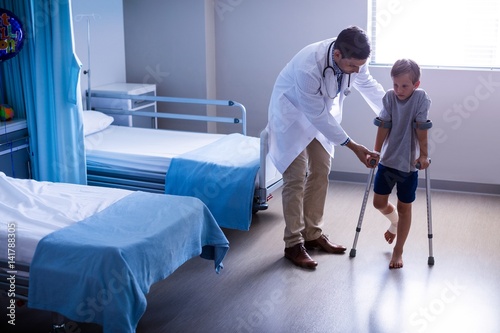 Canvas Print Doctor assisting injured boy to walk with crutches
