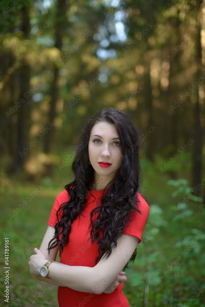 A beautiful model girl dressed in a red dress is standing in a mystical forest alone A beautiful model girl dressed in a red dress is standing in a mystical forest alone