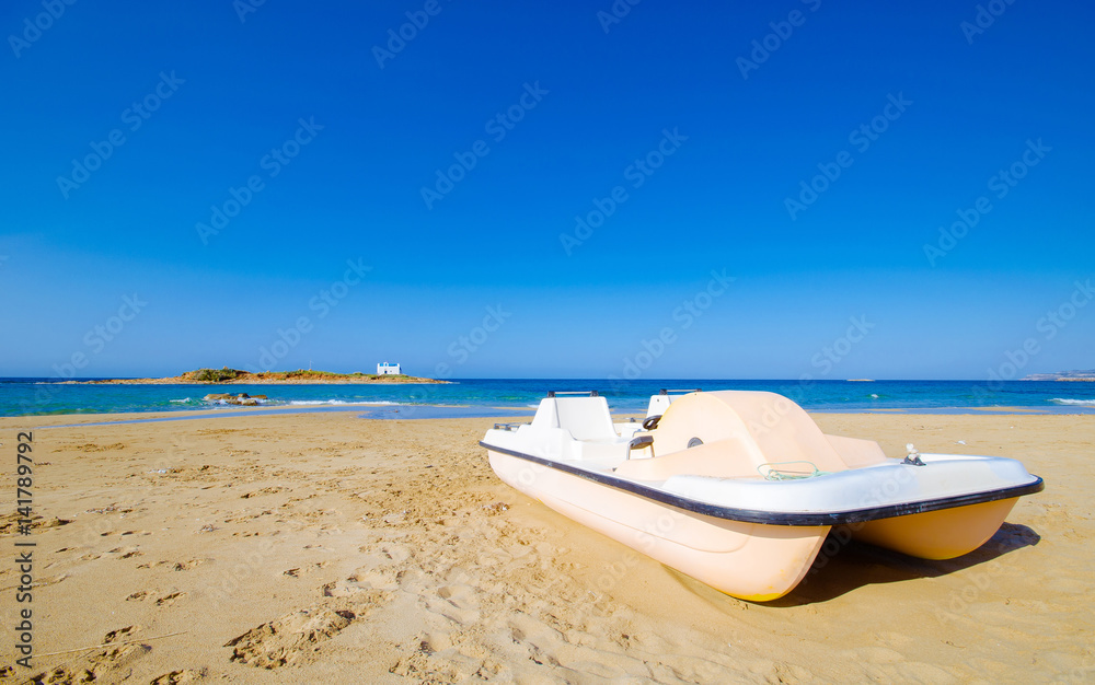 Typical summer image of an amazing pictorial view of a sandy beach with a boat on the beach and an old white church in a small island at the background, Malia, Crete, Greece.