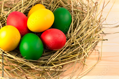 Easter eggs, painted in green, red, yellow, lie in a nest of hay