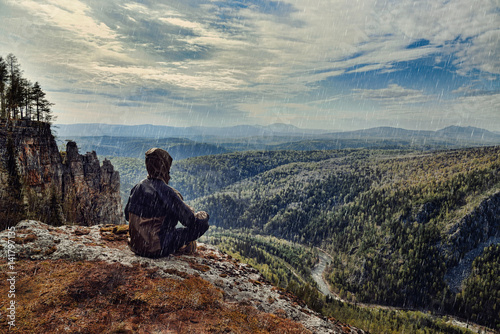 Man hiker sitting on top of mountain in rainy day, it is wet bad weather.