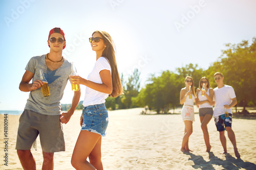 boy and a girl are holding bottles of beer in hands and smiling .Group of friends hanging out with beer at the beach. Excellent sunny weather. Beautiful figures. Super mood. Summer concept 