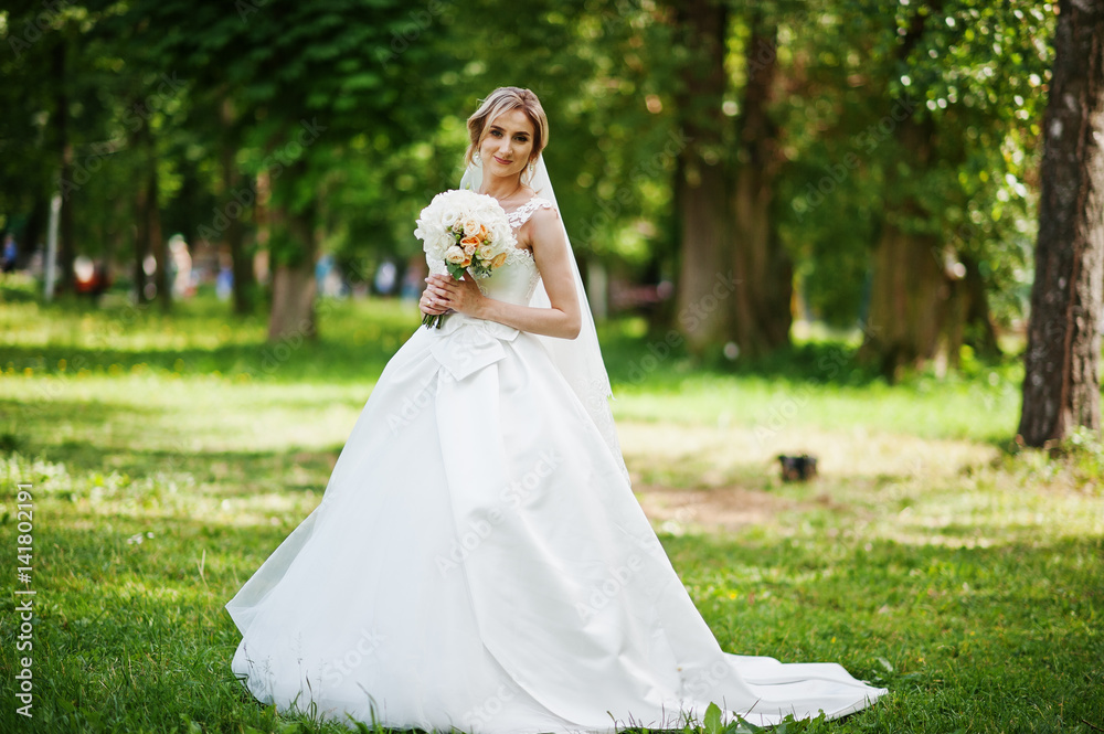 Cute blonde bride with wedding bouquet at park on sunny day.