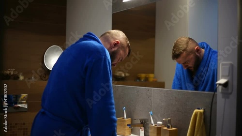 Worried man wearing bathrobe and having some problems while looking to the mirror
