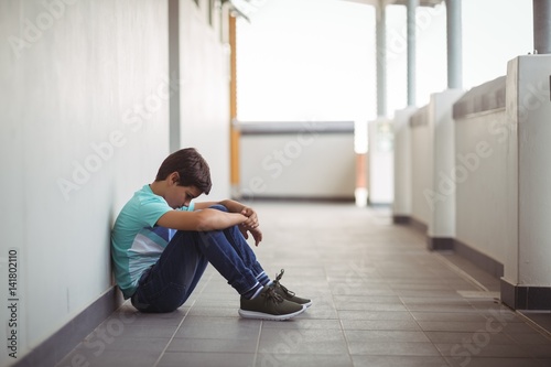 Foto Sad schoolboy sitting in corridor