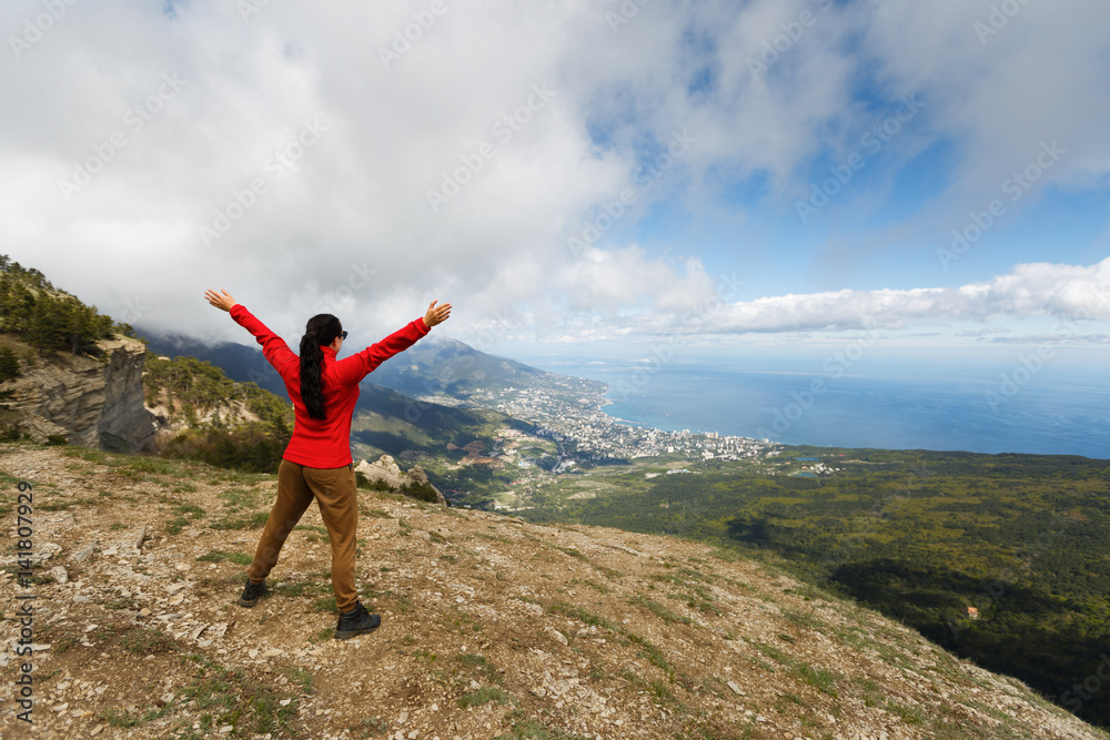 Cheering woman hiker open arms at mountain peak,Young girl spreading hands with joy and inspiration facing the Yalta city, Girl enjoying the freedom on mountain