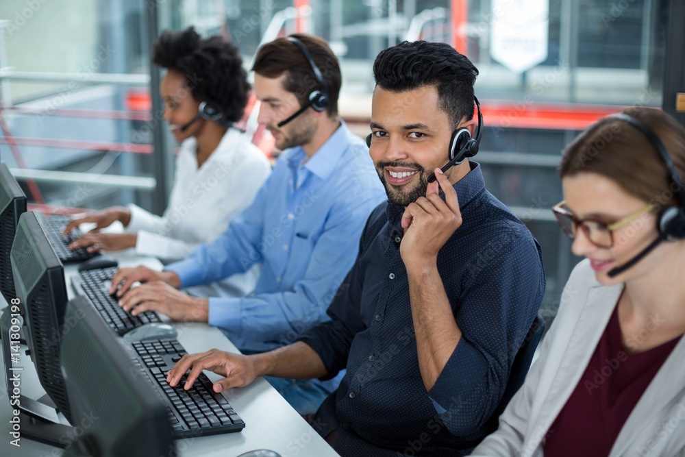 Business executives with headsets using computers at desk in office Business executives with headsets using computers at desk in office