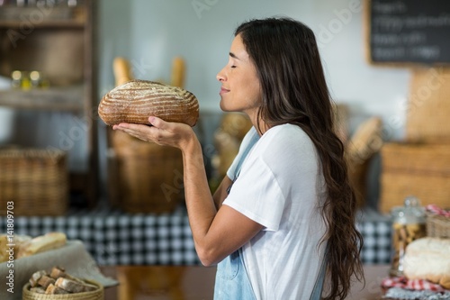 Smiling woman smelling a round loaf of bread at counter photo