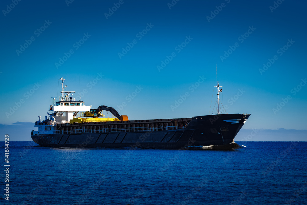 Black cargo ship with long reach excavator moving by baltic sea