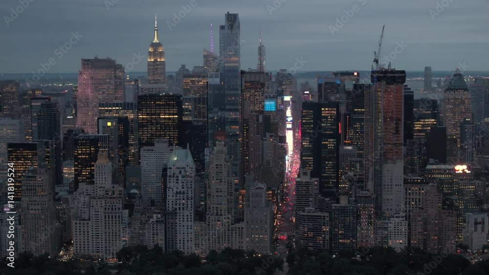 AERIAL COPYRIGHT FREE: Flying above illuminated New York City at dusk. Busy avenues opening up under high glassy skyscrapers, downtown Manhattan cityscape shining against the morning sky in background