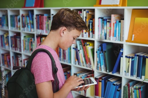 Attentive schoolboy using digital tablet in library