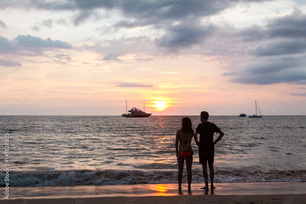 A couple looking at the ships. A couple standing on the shore and looking at the cruising ships. Horizontal outdoors shot.