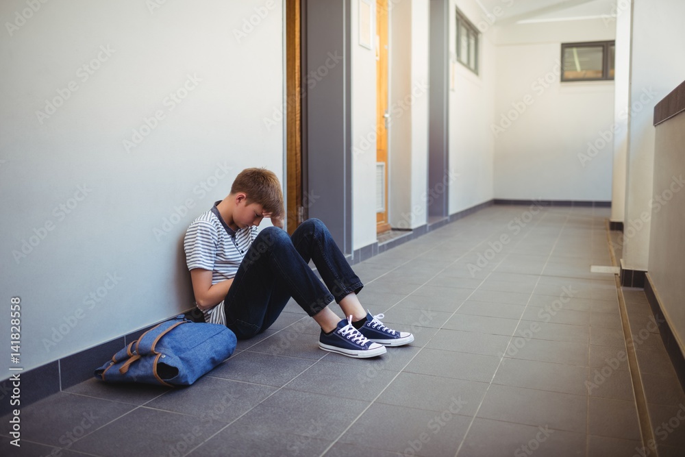 Sad schoolboy sitting in corridor