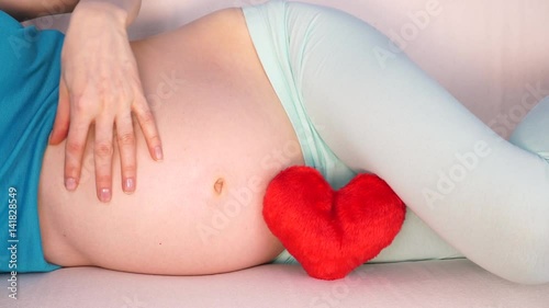 Wallpaper Mural Pregnant woman future mother lying on couch with red heart love symbol, caressing her naked belly. Pregnancy, motherhood and baby anticipation concept. 4K ProRes HQ codec Torontodigital.ca