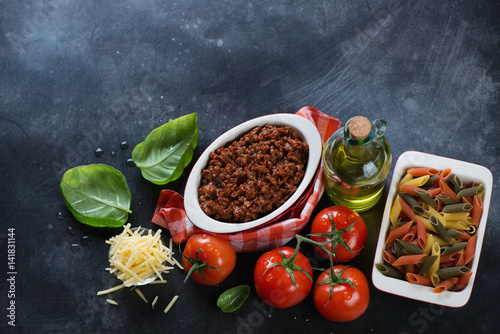 Bolognese sauce with raw penne pasta and other cooking ingredients on a scratched metal background, above view, copyspace
