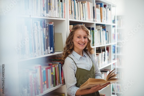 Portrait of happy schoolgirl reading book in library