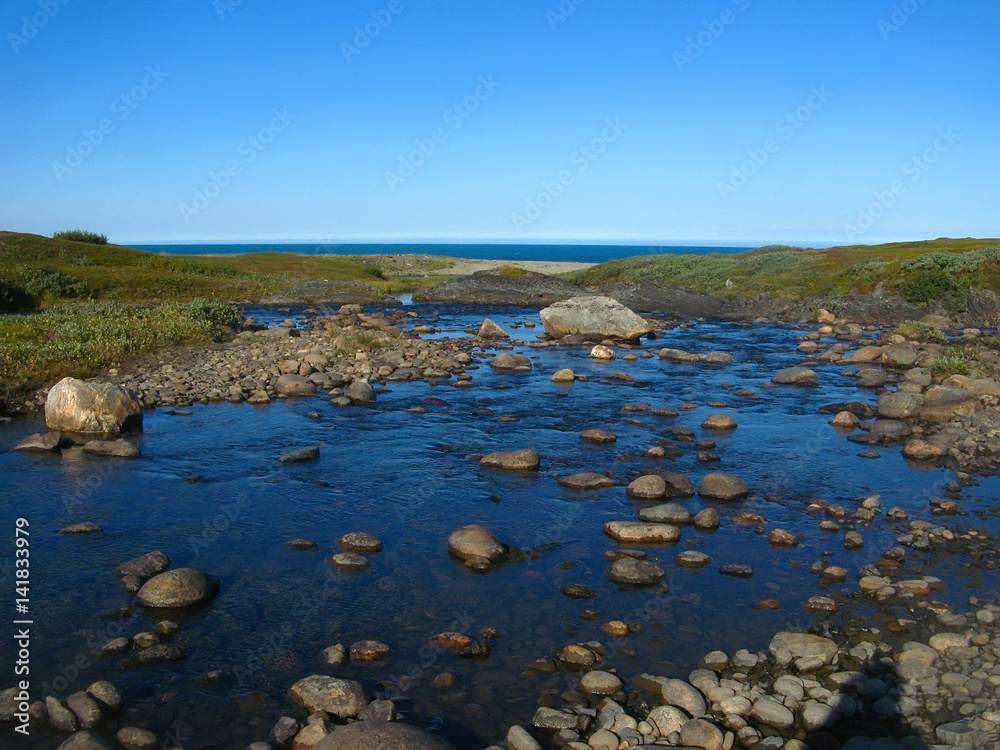 Background blurred view landscape shallow river flowing over the plateau and flowing into the Barents Sea on the Rybachiy peninsula, Murmansk region