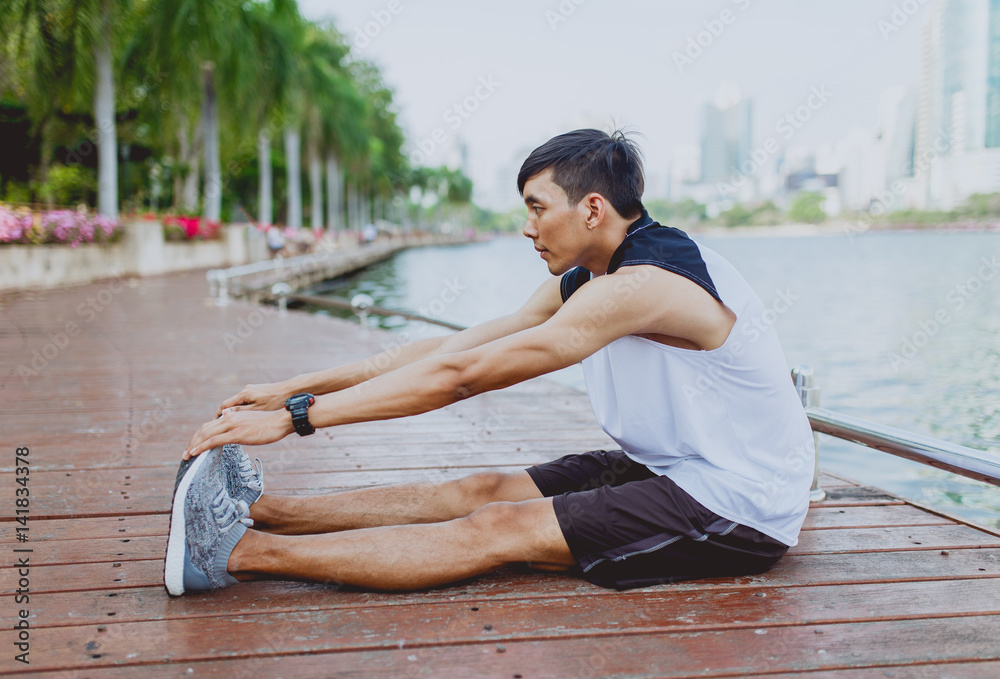 Young man stretching bodies, warming up for jogging in public park.
