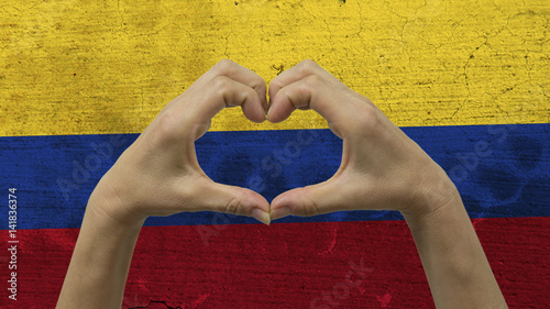 With a stylized Colombian flag background an anonymous person's hands being held in the form of a heart, symbolizing love and patriotism for Colombia.
