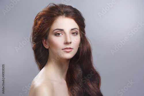 Beauty portrait of a cute girl with long chic hair isolated on a gray background.