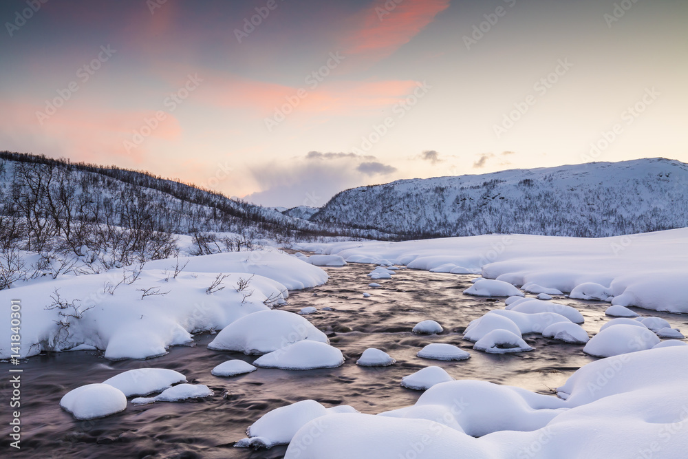 Water stream with rocks in a winter landscape in twilight.