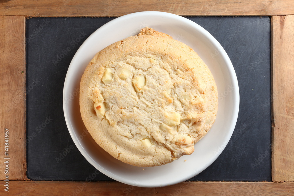 The white chocolate chip cookie on white dish put on slate board represent the pastry and bakery snack concept related idea. The white chocolate chip cookie on white dish put on slate board represent the pastry and bakery snack concept related idea.