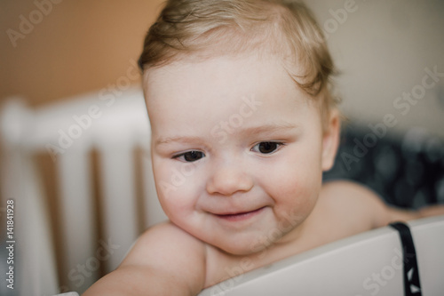 Happy cute baby boy smiling and sitting in the crib, just woke up