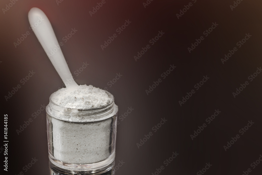 White powder in a transparent jar with a measuring spoon on a black background White powder in a transparent jar with a measuring spoon on a black background