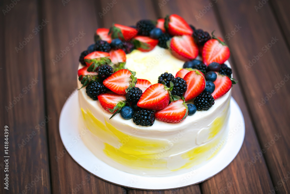 Birthday lemon cake with strawberries, blueberries and blackberries on a dark wooden board Birthday lemon cake with strawberries, blueberries and blackberries on a dark wooden board