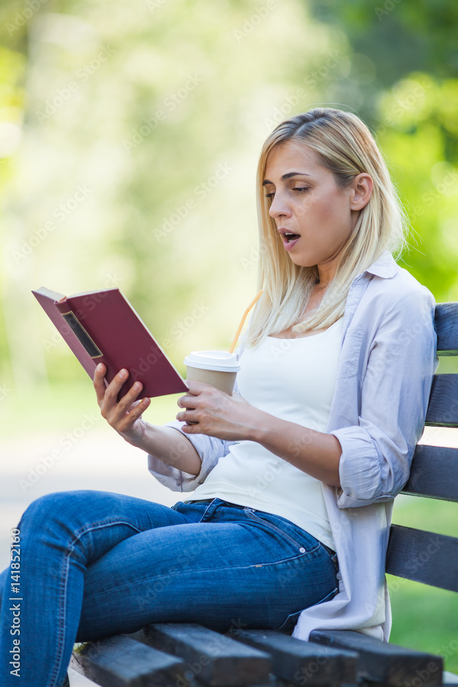 Obraz premium Young woman is sitting in park and reading book.