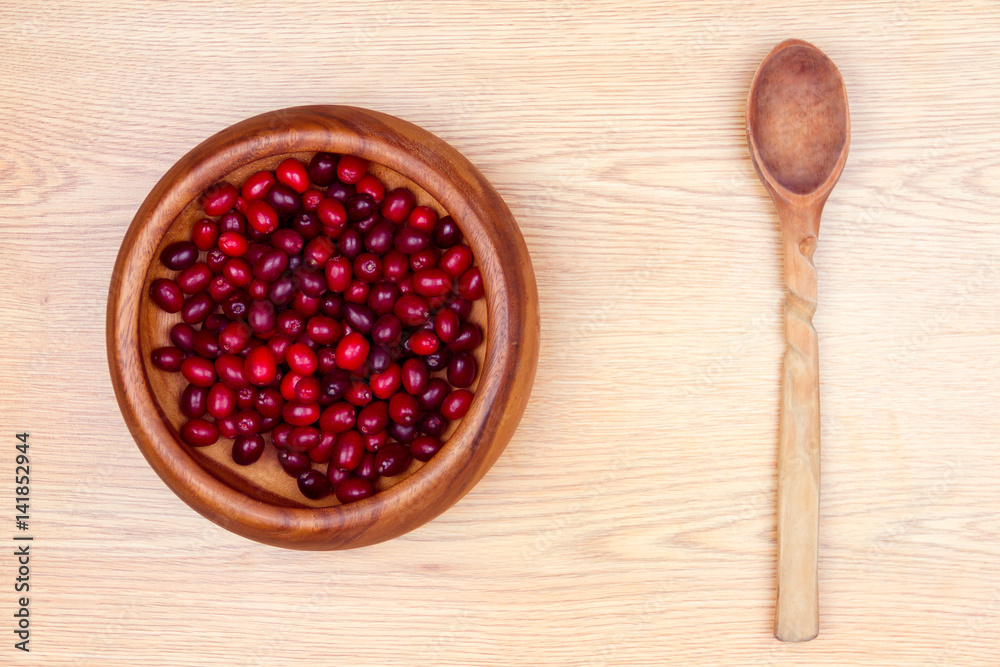 Healthy food. Wooden plate with fresh cornel in it and wooden spoon isolated on beige background. Healthy food. Wooden plate with fresh cornel in it and wooden spoon isolated on beige background.