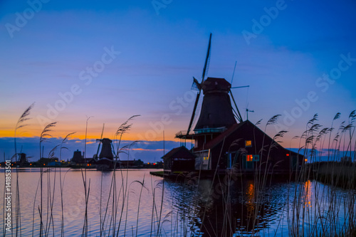 Sunset landscape with windmills and field wild herbs and flowers. Silhouettes of Dutch mills near the lake at sunset in a rural landscape. Sunset in landscape with mill the Netherlands. Dutch mills.