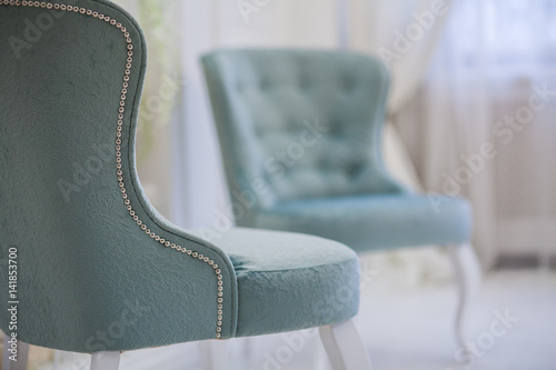 Two turquoise classic luxury armchair in white room. One mint chair standing back to camera. Close-up.