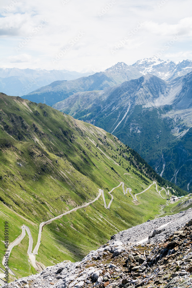 Alp road surrounded by blue alp high mountains and green hills. Steep descent of Passo dello Stelvio in Stelvio Natural Park, Tyrol, Italy.