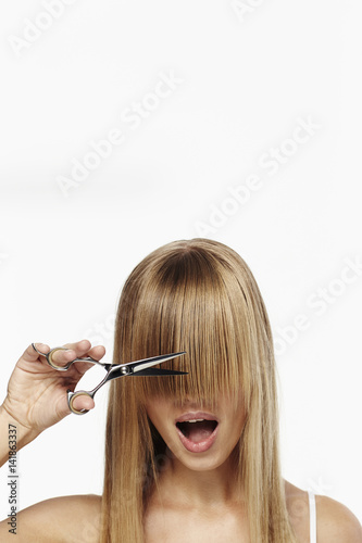 Blond girl with scissors about to cut fringe, studio