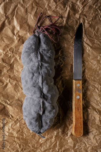 Sausage salami and knife on beige paper top and side view. Sausage sausage with ashes. French country sausage. Rustic food still life © beverli