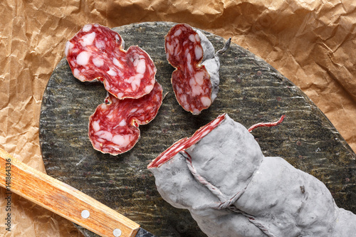 Sausage salami and knife on beige paper top and side view. Sausage sausage with ashes. French country sausage. Rustic food still life