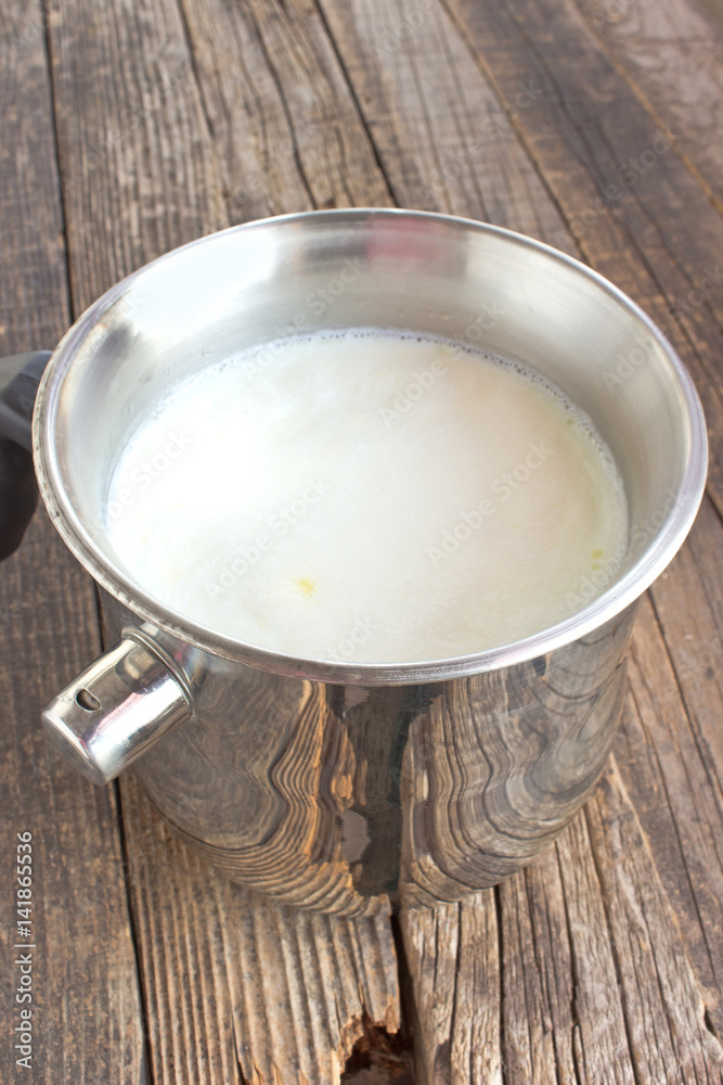 Hot milk boiled in metal pot with whistling alarm on wooden table Hot milk boiled in metal pot with whistling alarm on wooden table