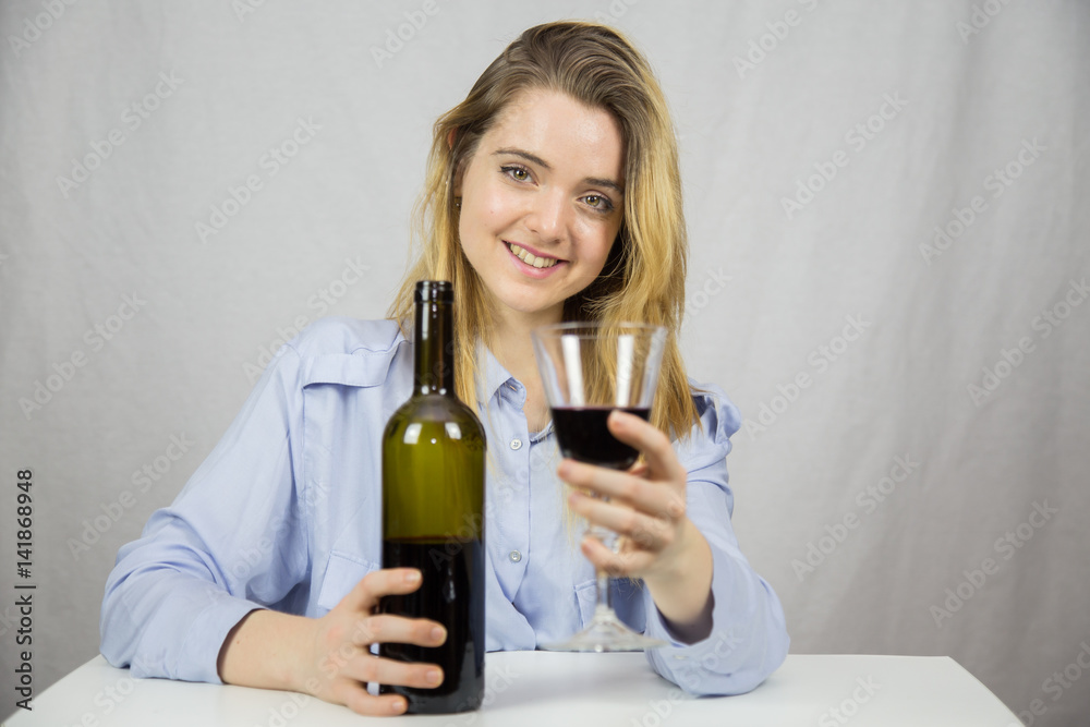 Young Caucasian white woman sitting at a table while drinking wine. She is blonde and pretty with light brown eyes. The background of the image is white. Young Caucasian white woman sitting at a table while drinking wine. She is blonde and pretty with light brown eyes. The background of the image is white.
