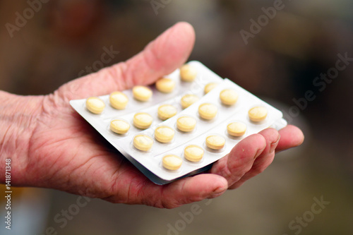 Old woman holding pills in her hand. Elderly female hand with pills or pharmaceutical meds. photo