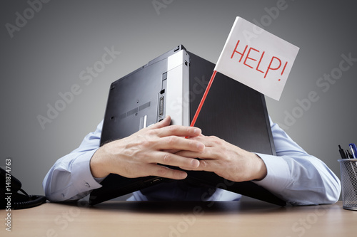 Businessman burying his head uner a laptop asking for help photo
