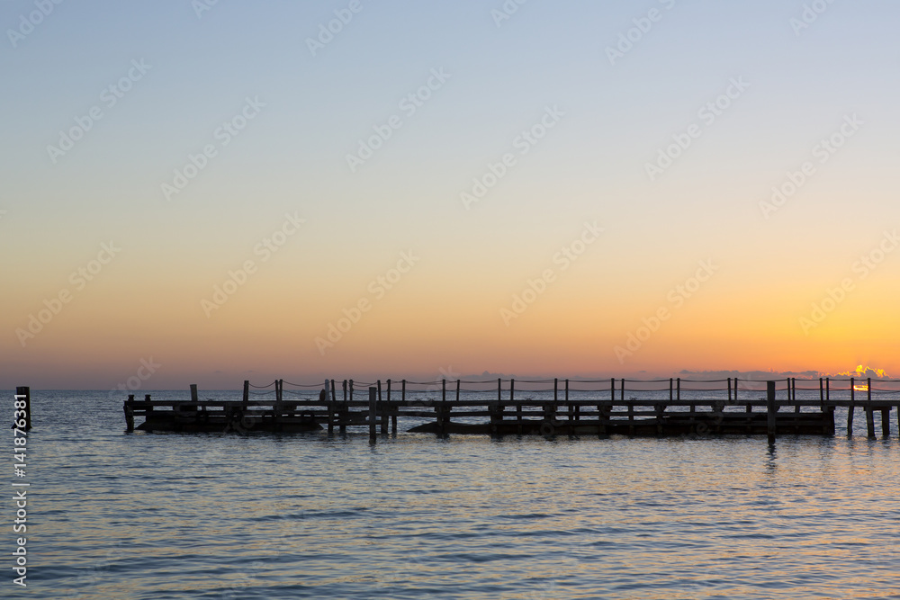 Beautiful sunrise on a wooden pier in the shores of Caribbean sea. Silent beach. Peaceful. Sun is rising behind the silhouette dock.