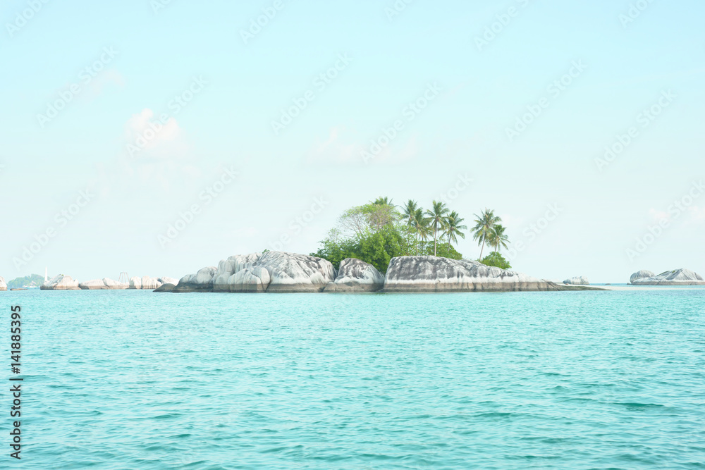 Natural rock formation in sea with green palm trees and vegetation on top at Belitung Island in the afternoon and a white lighthouse at the background, Indonesia.